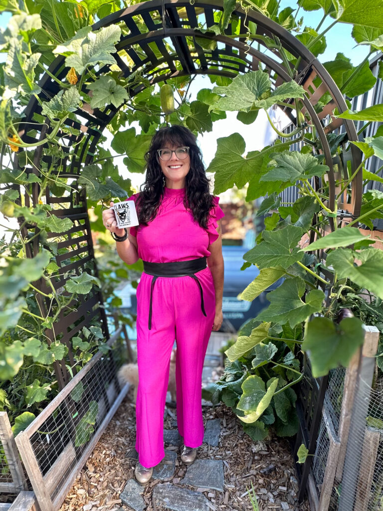 Rachelle looking fancy for the garden in a romper, drinking coffee under a squash arbor